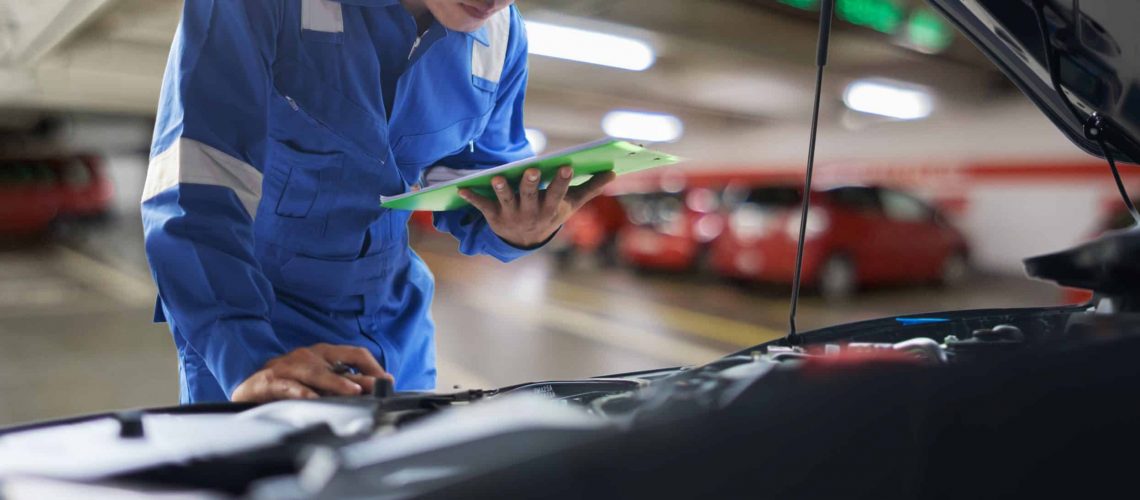 car service, repair, maintenance concept - Asian auto mechanic man or Smith writing to the clipboard at workshop warehouse, technician doing the checklist for repair machine a car in the garage,banner